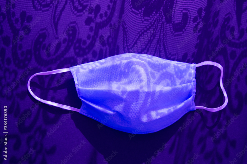 Fototapeta premium Medical mask againts virus covid-2019 in the sunlight with ornament shadows. Dark purple neon tone on a dark background. Heath care concept, stop coronavirus
