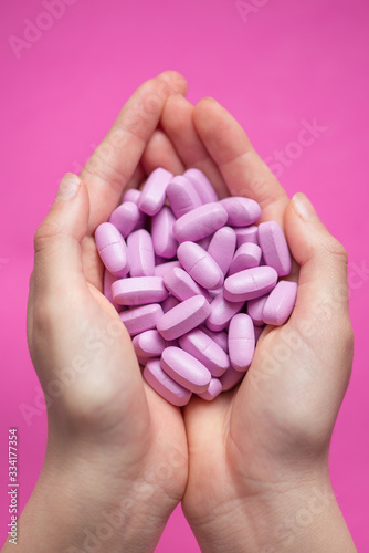 Hands holding plenty of pink pills  tablets  over pink background