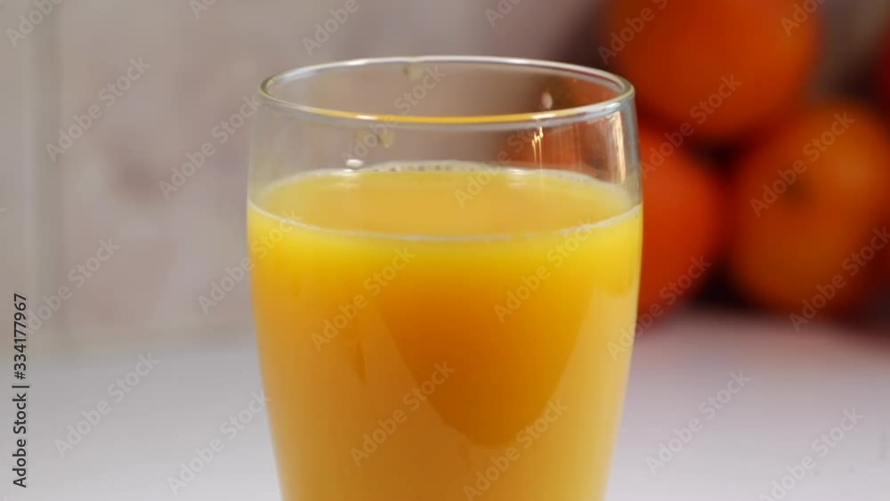 Orange juice is poured into a tall glass, on a white kitchen table with tangerines, in the kitchen. Orange juice is poured into a tall glass, on a white kitchen table with tangerines, in the kitchen.