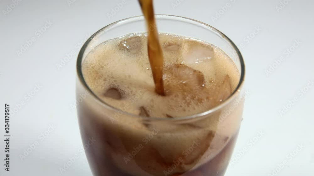 Refreshing cola is poured into a glass of ice. Icy beverage of cool drink with caffeine. Cold glass with cola and ice is on the kitchen table. Refreshing cola is poured into a glass of ice. Icy beverage of cool drink with caffeine. Cold glass with cola and ice is on the kitchen table.