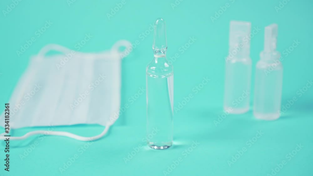 hand in surgical gloves puts a glass ampoule with a vaccine on a blue surface next to a medical protective mask hand in surgical gloves puts a glass ampoule with a vaccine on a blue surface next to a medical protective mask