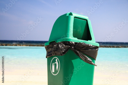 Leinwand Poster Green Plastic Flap Bin on Clean Sandy Tropical Beach after Recycling Waste