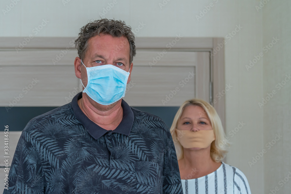 a older couple wearing mask to prevent coronavirus, he a medical mask she a tape for the mouth to be quiet