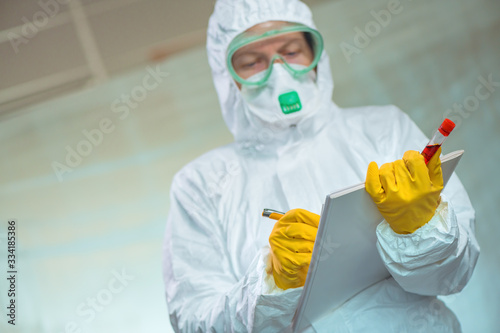 Virologist with blood test sample lab tube writing notes