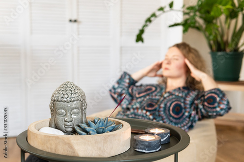 Young blonde woman meditating at home with candle lights and incense stick on foreground
