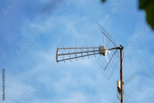 A rusty UHF television antenna was photographed from a distance against the blue sky background.