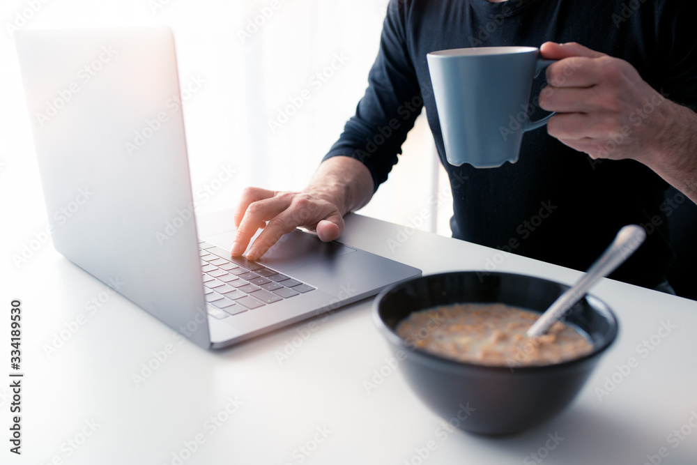 Middle-aged Caucasian man having breakfast while working from home, using his laptop, due to covid-19 coronavirus. Middle-aged Caucasian man having breakfast while working from home, using his laptop, due to covid-19 coronavirus.