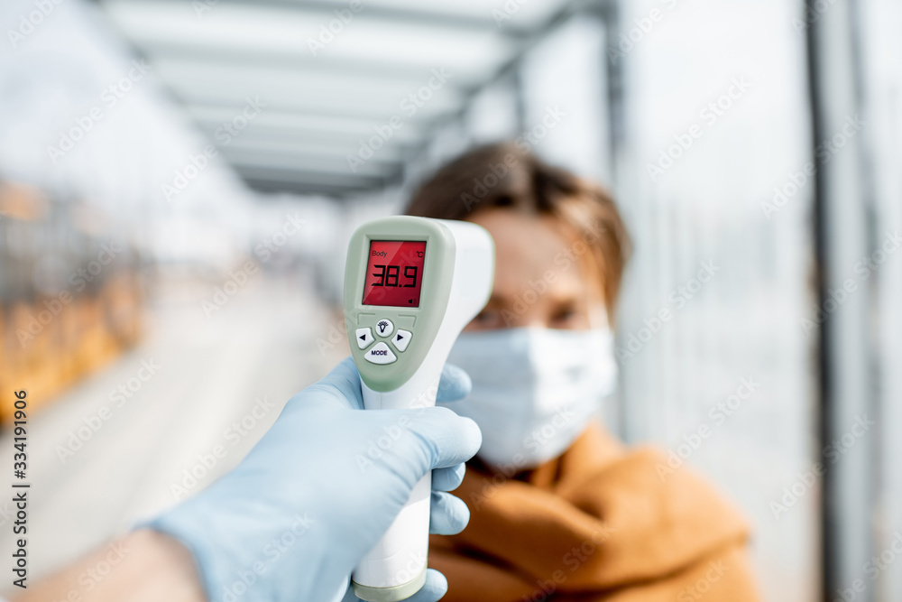 Measuring temperature with infrared thermometer of a young woman in face mask at a checkpoint during an epidemic outdoors. Concept of prevention the spread of the virus