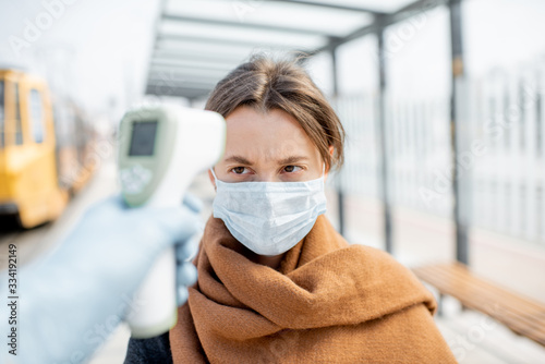Measuring temperature with infrared thermometer of a young woman in face mask at a checkpoint during an epidemic outdoors. Concept of prevention the spread of the virus