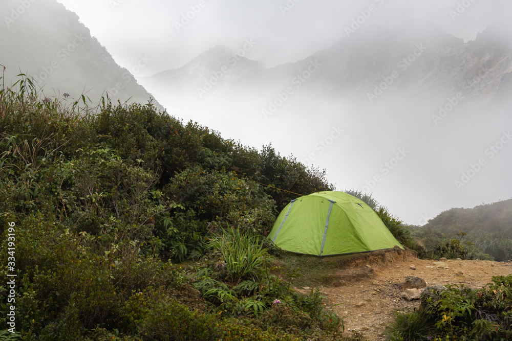 Green tourist tent on a background of mountain peaks in the fog. Copy space