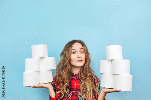 Girl with a lot of rolls of toilet paper in her hands on a blue background. Lack of toilet paper during the coronavirus pandemic. Lack of hygiene products.