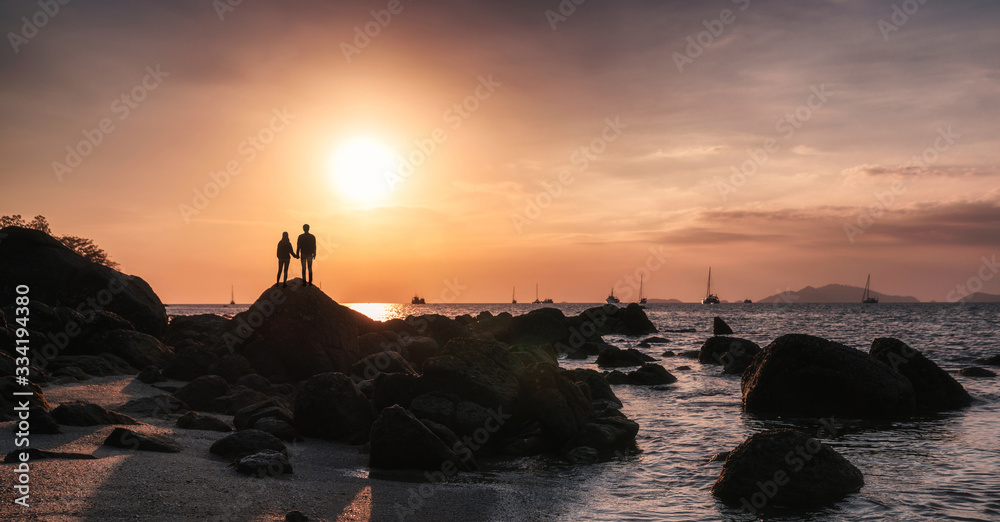 Young couple looking the sunset on coastline in tropical sea