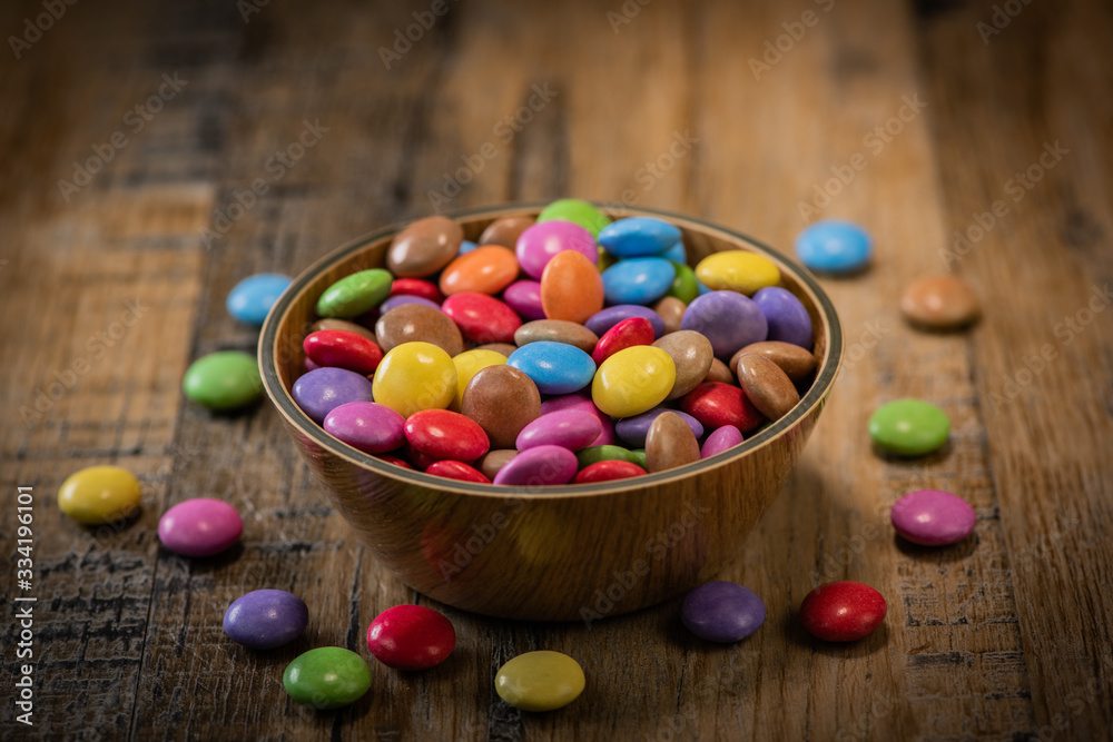 Colorful candies in a wooden bowl case isolated on wood background Colorful candies in a wooden bowl case isolated on wood background