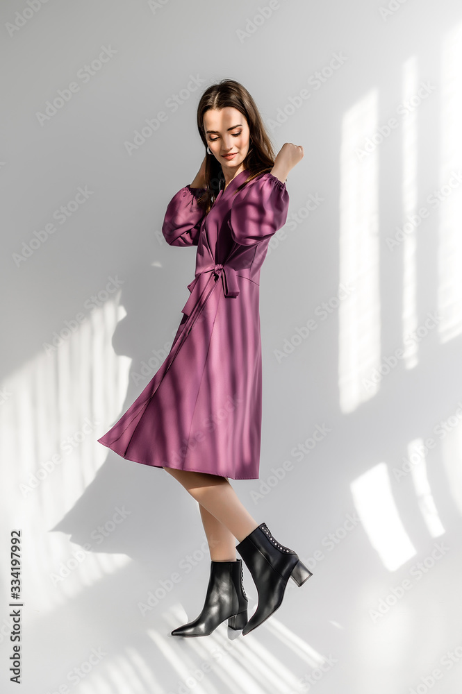 Attractive brown-haired woman in a purple checkered dress on a white background. Photosession for a clothing catalog Attractive brown-haired woman in a purple checkered dress on a white background. Photosession for a clothing catalog