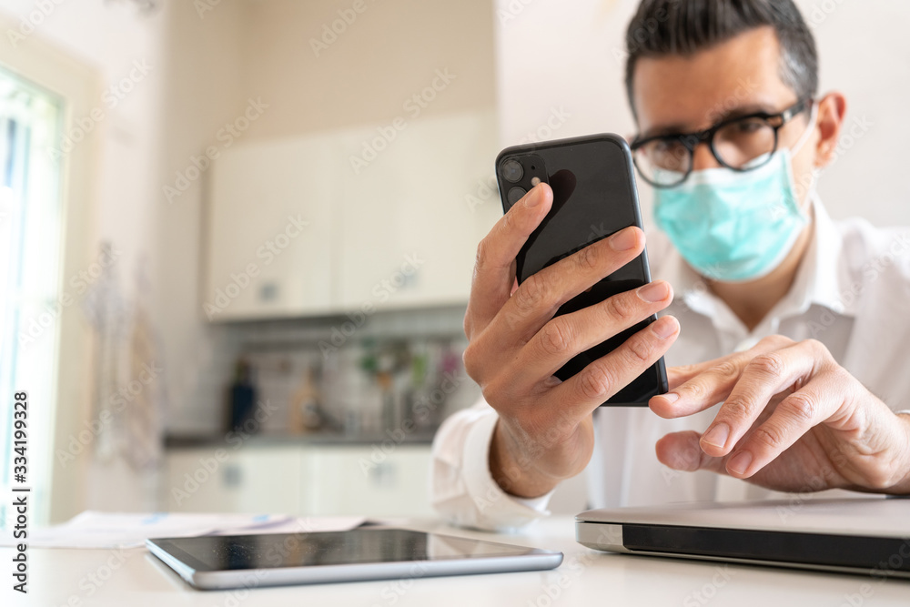 Man using a smartphone working at home during corona virus wearing a medical mask Man using a smartphone working at home during corona virus wearing a medical mask