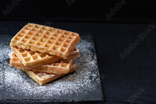 Sweet tasty Belgian waffles close-up, sprinkled with powdered sugar