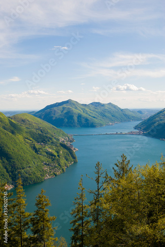 A top view of Lake Lugano, Switzerland from the height of Mount Monte Bre. Beautiful mountain scenery on a sunny summer day. View of Lake Lugano and the Alpine mountains covered with green plants.