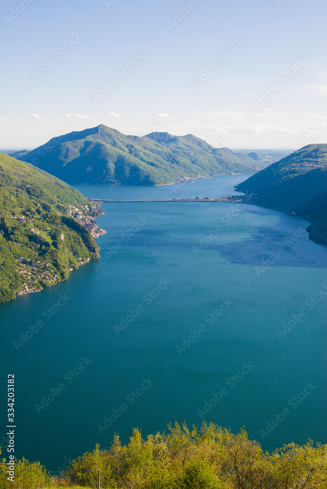 Naklejka premium A top view of Lake Lugano, Switzerland from the height of Mount Monte Bre. Beautiful mountain scenery on a sunny summer day. View of Lake Lugano and the Alpine mountains covered with green plants.