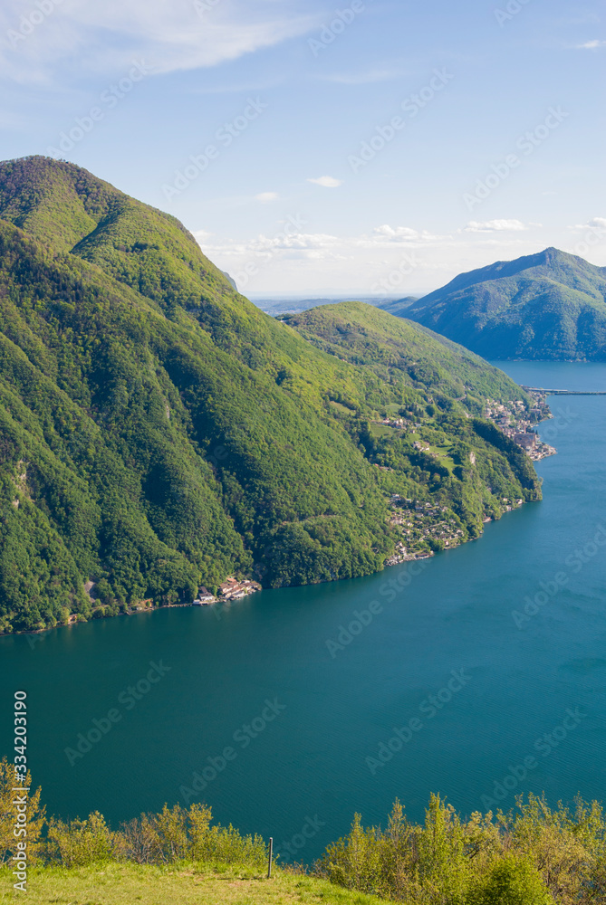 A top view of Lake Lugano, Switzerland from the height of Mount Monte Bre. Beautiful mountain scenery on a sunny summer day. View of Lake Lugano and the Alpine mountains covered with green plants.