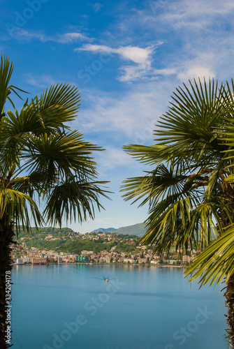 View of the lake and the city of Lugano on a sunny summer day, Switzerland. Palm trees at the sides of the frame.