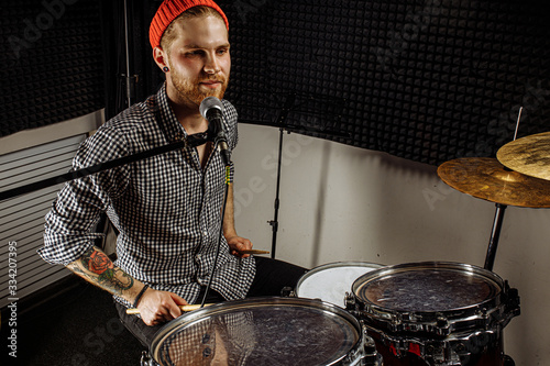 talented caucasian musician contemporaneously going to play on drums and sing on microphone. professional drummer preparing for rock concert, practice in dark studio. music concept photo