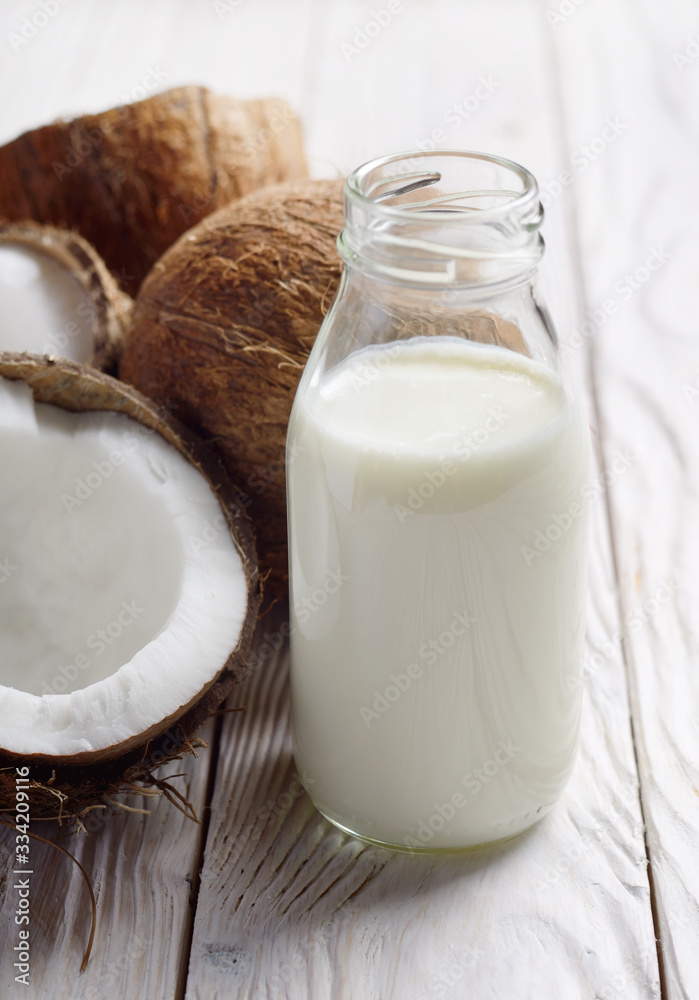 Glass bottle with milk or yogurt on white wooden kitchen table with coconut aside Glass bottle with milk or yogurt on white wooden kitchen table with coconut aside