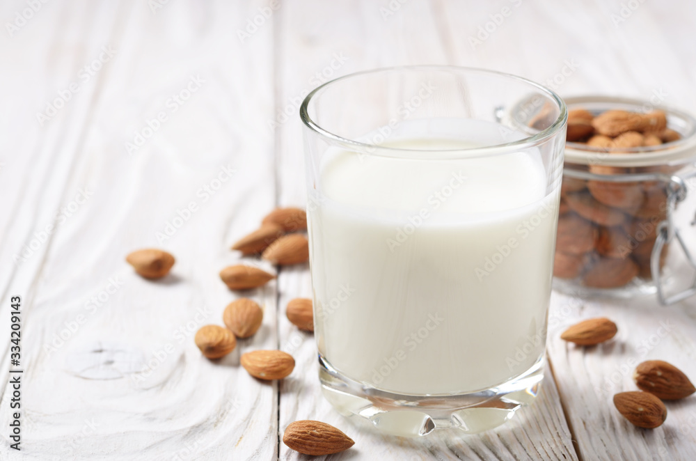 Milk or yogurt in drinking glass on white wooden table with almonds in airtight conainer aside