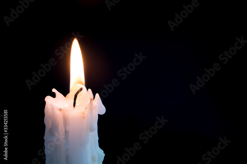 Candleflame on a lit candle. White candle burning, isolated on a dark background