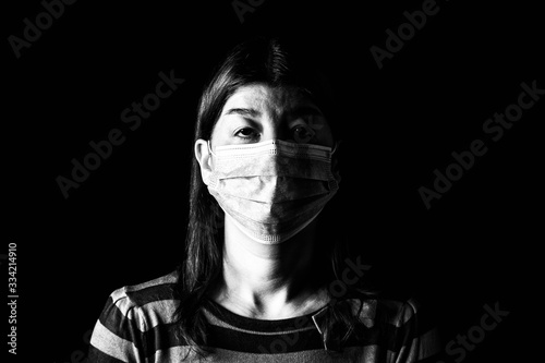 Woman with surgical mask. Pandemic or epidemic and scary, fear or danger concept. Protection for biohazard like COVID-19 aka Coronavirus. Black and White. Black Background