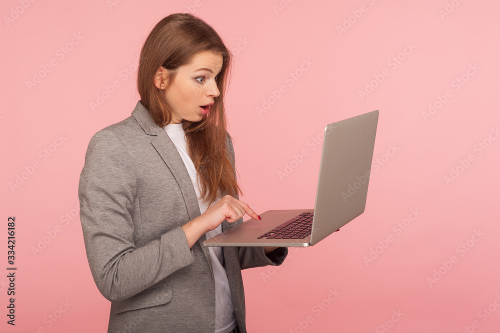Portrait of office employee typing on laptop and looking with amazed expression, businesswoman using computer to study, working online, shocked by application. studio shot isolated on pink background