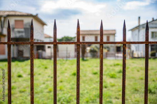 View of old rusty fence with thin sharp peaks on village blur background