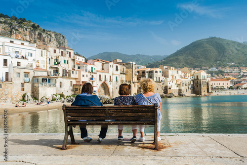 Women sit on a bench and enjoy the view of the coastal city of Cefalu, Sicily, Italy