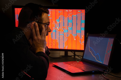Silhouette of a young man in front of a computer with graphics and numbers in red because of the crisis. Selective focus