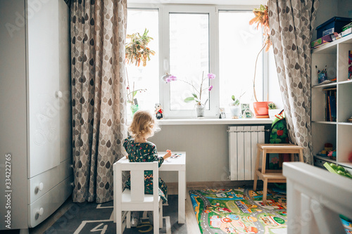 child sitting at the table in the kids room near the window. back view photo