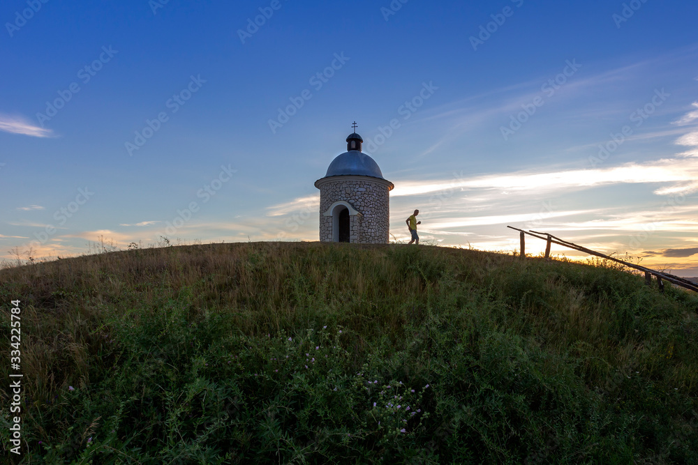 Stone chapel Hradistek at sunset with beautiful blue sky in the foreground green grass with pink flowers Stone chapel Hradistek at sunset with beautiful blue sky in the foreground green grass with pink flowers