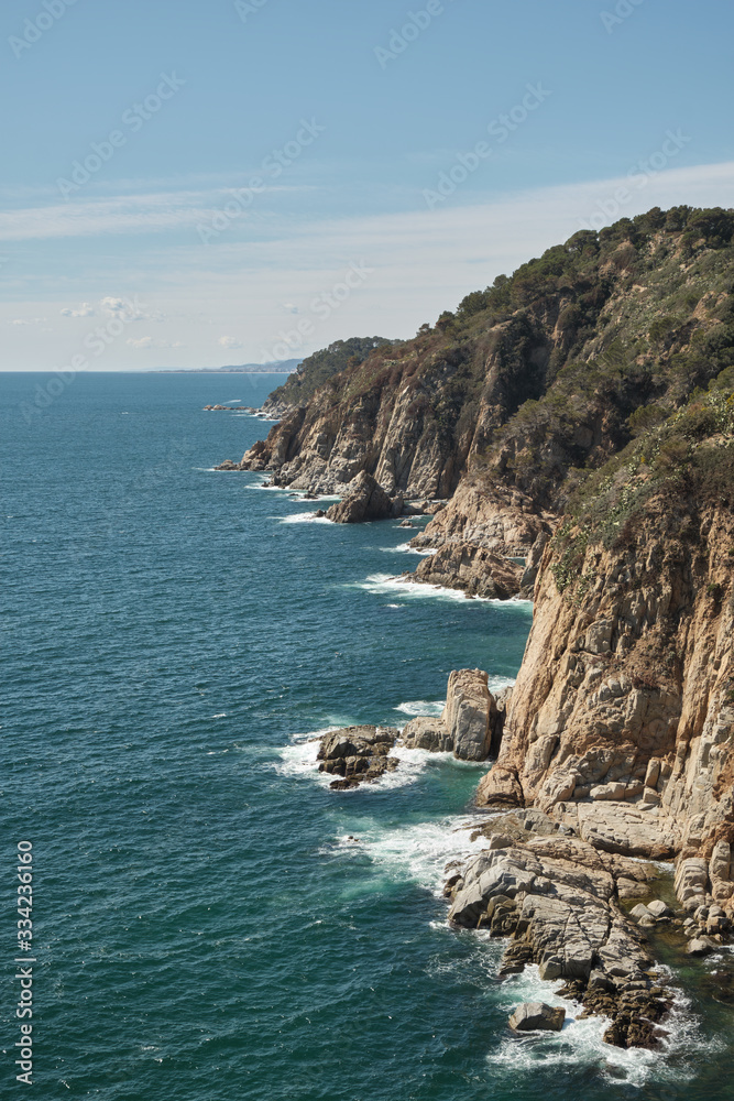 Holes breaking on the rocks of cliffs on the Mediterranean sea on a sunny day, Costa Brava, Tossa de Mar, Catalonia, Spain.