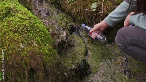 Close-up of A female hiker filling clean, fresh drinking water into a plastic bottle from a mountain spring.