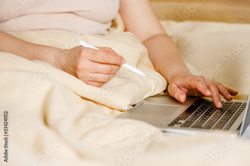 Mobile Office at home or remote work. Adult woman in pajamas in bed at home working using on laptop computer. Freelance business quarantine concept