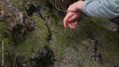A woman washes her hands in a crystal clear mountain spring close up.