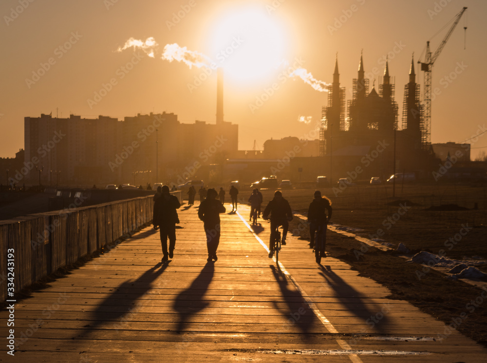 People walking on the street in the city at golden sunset. Four silhouetts opposite the setting sun. Nizhnevartovsk embankment.