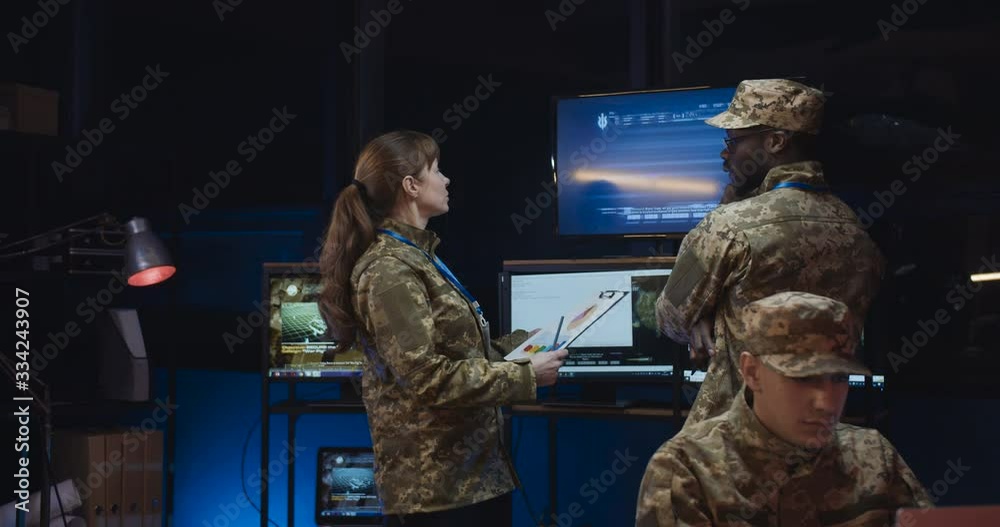 Caucasian woman militarian official coming to African American male general and bringing new information and data in documents about conflct in war zone. Man watching troops dislocation in office.
