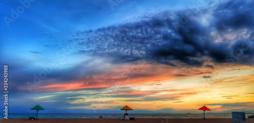 beautiful sunset on the beach of lake with dramatic sky with no people. Colourful sky blue  orange  red  grey  yellow  black. Three beach umbrella. 