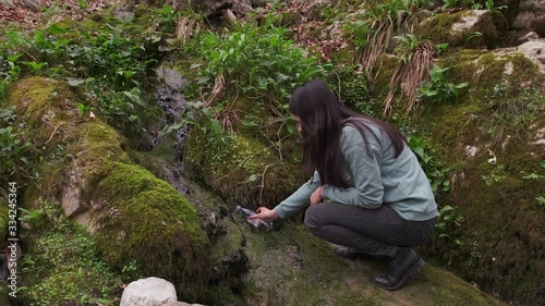 A female hiker fills clean, potable water in a plastic bottle from a mountain spring. A girl fills a bottle with water from a mountain stream.