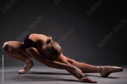 Ballerina sitting in a pose bowed her head against a gray background