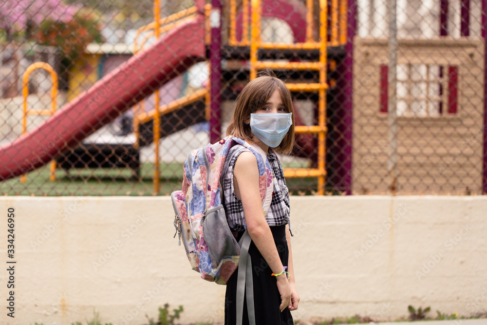 A school aged girl is longing to attend her closed school. She is in front of her school with a facemask on during the covid-19 outbreak. A school aged girl is longing to attend her closed school. She is in front of her school with a facemask on during the covid-19 outbreak.