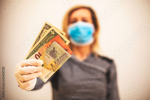 Woman in medical protective mask and transparent protective gloves counts money