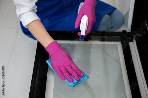 A girl in pink rubber gloves washes an oven with a rag and detergent with a spray.