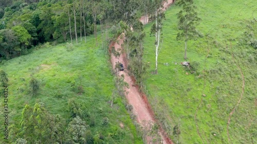 Aerial view of car driving throuh a small dirt road in the middle green tropical valley and farmland. Brazil photo