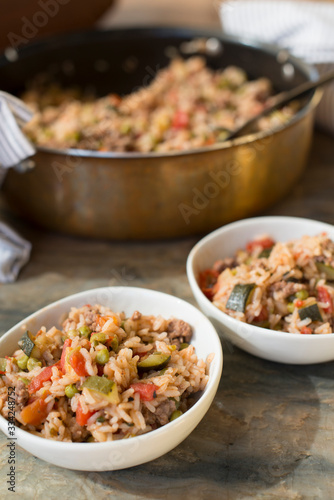 A casserole with rice and tomatoes and beans made in a copper pot and served in white dishes for a healthy meal