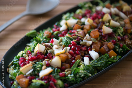 Winter salad with pomegranates, pears, kale sweet potato and pumpkin seeds served on a black serving plate in a beautiful setting